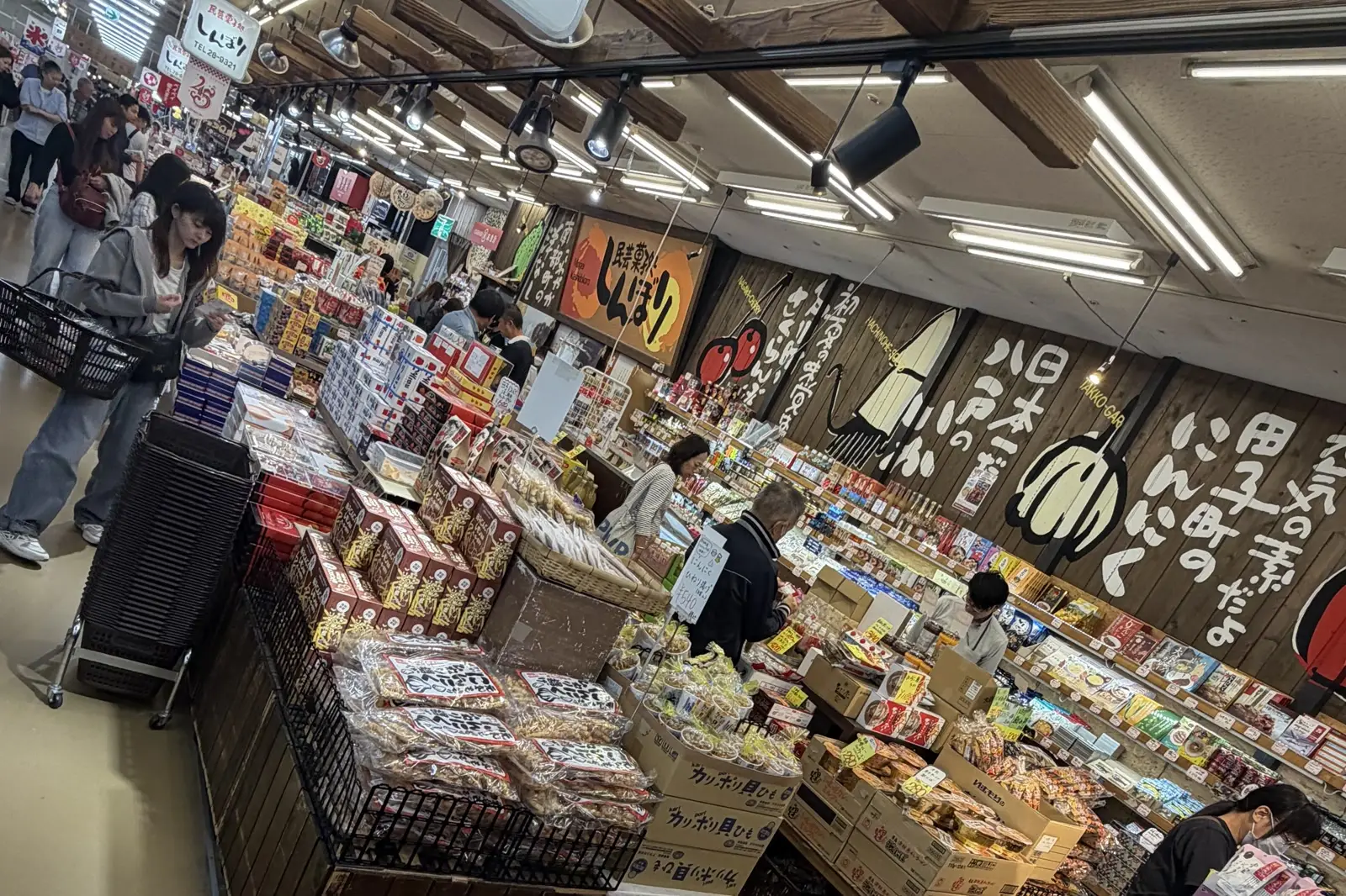 買い物客で賑わう八食センターの売場。木の壁一面に八戸名物の看板が並ぶ