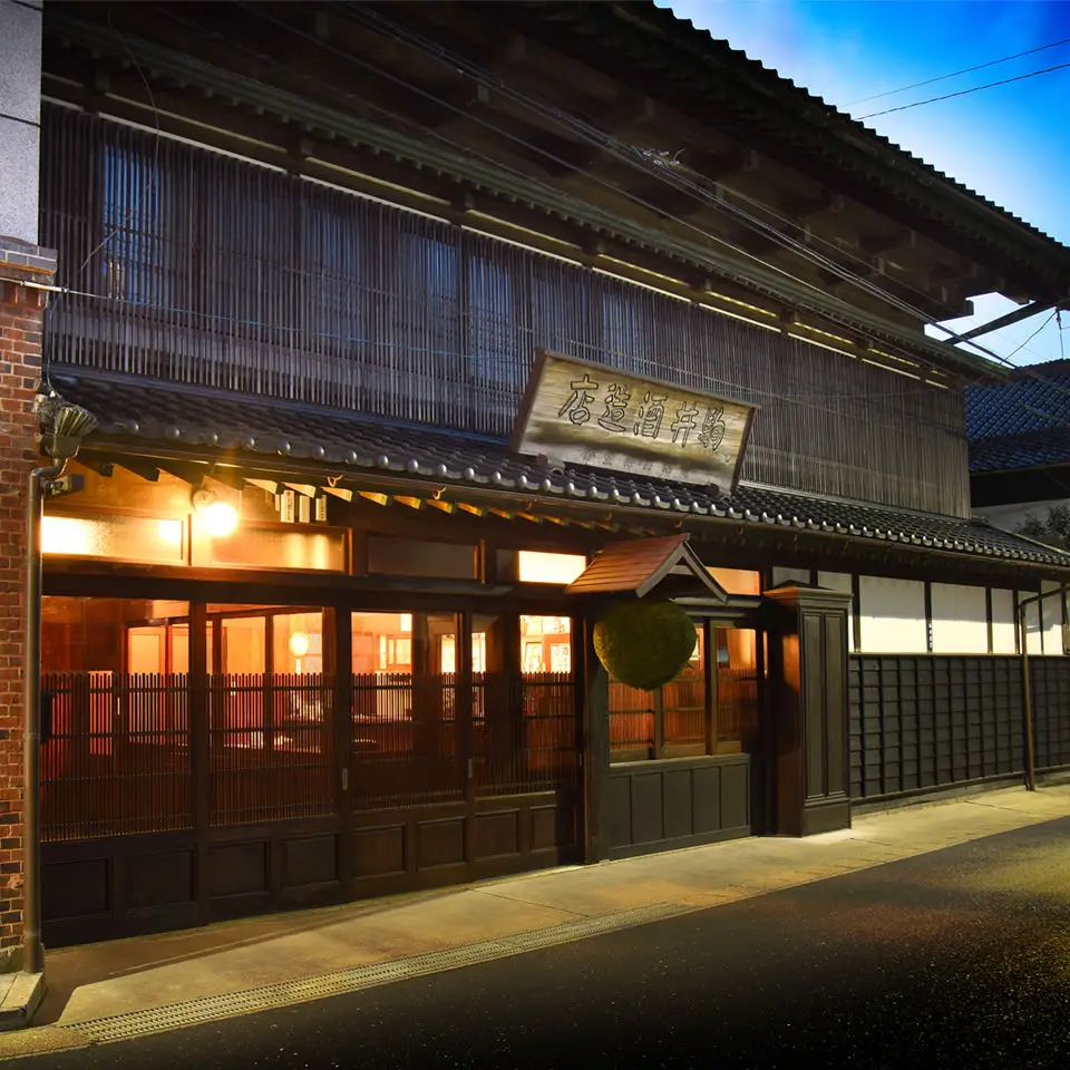 夕暮れどきの八戸酒造。灯りのともる木造の蔵構え