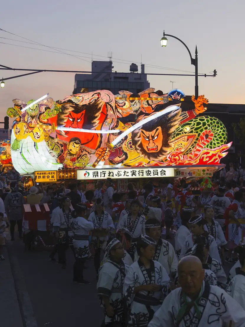 夕暮れの青森市内。囃子方の列の先で大型ねぶたが灯る